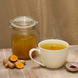 Organic Sano Turmeric & Saffron Chicken Broth in a mug with fresh turmeric and saffron